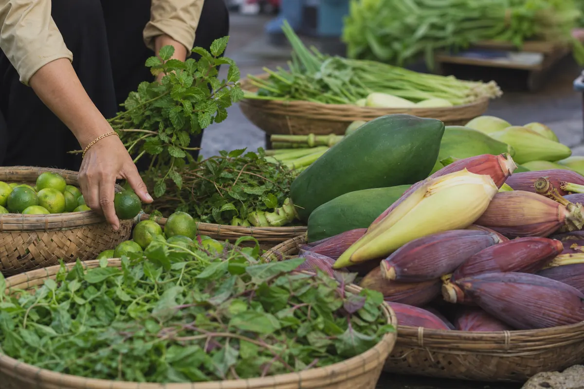 Fresh herbs, banana blossom, green papaya and limes arranged at a morning market